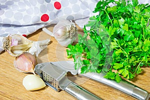 Crushing garlic to add to the dish. Whole and chopped garlic on a cutting Board made from natural oak. Fresh parsley.