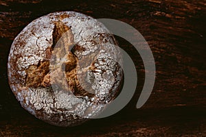 Crusty round loaf of healthy whole grain bread on dark wooden table background with white flour on top. top view of buckwheat