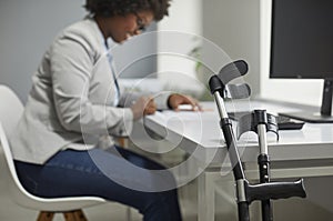 Crutches by office desk with happy disabled female employee working on computer in background