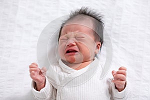 Crying and angry Newborn baby boy lying on white bed at home.Infant baby screaming very hungry or stomach pain. sick asian baby