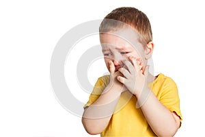 Crying baby boy in a yellow T shirt covers his face with hands and shouts, studio isolated on white background