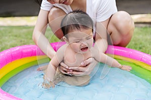 Crying baby carried by mother enjoying in Inflatable pool