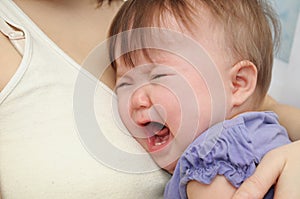 Crying baby at the mother on hands. Soothing upset child embracing and calming