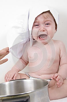 Crying baby wearing chef hat and with pan