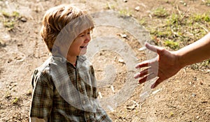 Crying capricious boy is sitting on the road, father provides hand. Parent Helping Hands.