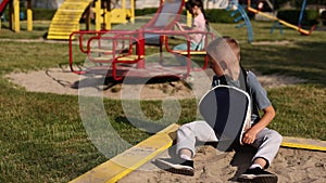 crying child with broken limb arm sits outdoors and looking how kid girl is playing on playground. concept of health