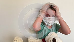 A crying child in a mask and latex gloves with a Teddy bear looks at the camera.