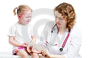 Crying child with scratched knee. Doctor provides first aid.