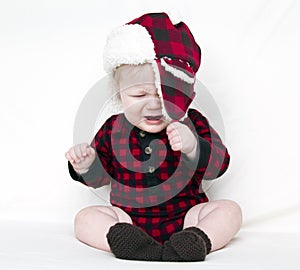 Crying Christmas baby trying to pull off hat