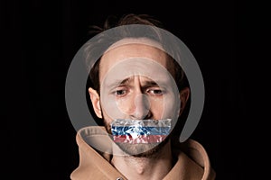 Close-up portrait of young emotive man with three colors duct tape over his mouth isolated on dark background