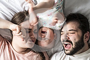 Crying couple and a little baby in bed at home
