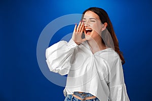 Crying emotional young woman screaming on blue studio background