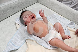 Crying newborn baby on changing table. Cute little girl or boy two weeks old. Dry and healthy body and skin concept