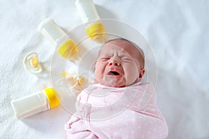 Crying newborn baby girl with nursing bottles. Bottle feeding