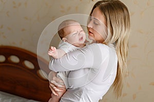 Crying newborn baby in mother& x27;s arms. Loving mom looks at child with love, calms her down, rocks baby in her arms in