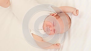 a crying newborn baby in a white bodysuit on a cotton bed screams and calls for his mother