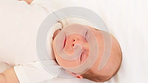 a crying newborn baby in a white bodysuit on a cotton bed screams and calls for his mother, close-up portrait
