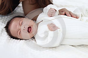 Crying newborn infant baby boy lying down on white on bed in white bedroom, mother gentle touching him, lovely family mom and