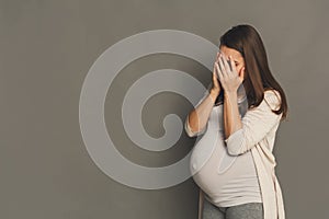 Crying pregnant woman, gray studio background