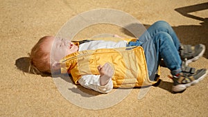 Crying and screaming baby boy lying on the ground on street. Upset children, negative emotions, kids problems