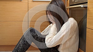 Crying teenage girl sitting on floor at kitchen. Mental problems and depression of teens