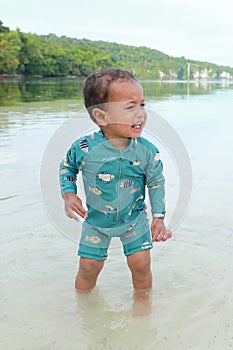 Crying toddler boy in blue swimsuit standing in shallow sea