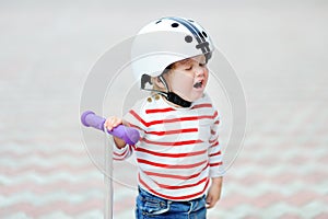 Crying toddler boy in safety helmet with scooter