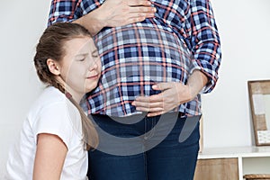 Crying unhappy daughter leaning belly of pregnant mother, child not wanting a sibling