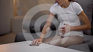 Crying unhappy pregnant lady counting coins on table and touching belly, poverty