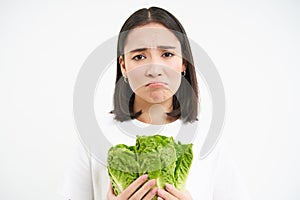 Crying woman holding vegetable, sitting on diet and eating cabbage instead of junk food, white background