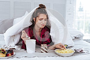 Crying woman lying in her bed surrounding by snacks