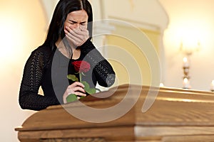 Crying woman with red rose and coffin at funeral