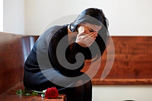 Crying woman with red rose at funeral in church