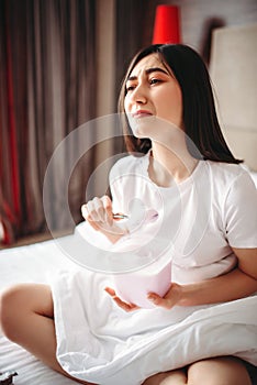 Crying woman sitting in bed and eats ice cream