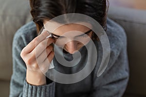 crying woman with tissue sitting on sofa at home