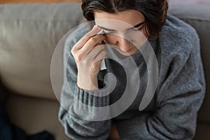 crying woman with tissue sitting on sofa at home