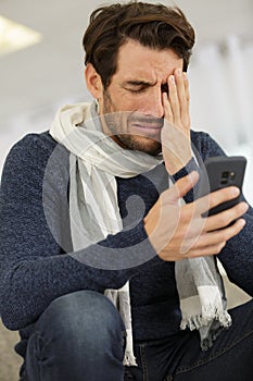 Crying young man looking at smartphone