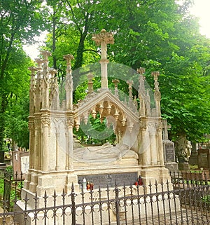 The crypt in which lies a man of high rank. Above it is a lot of columns. Around the green trees and grass.