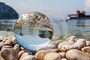 Crystal ball on pebbles near the sea. Original upside down view and rounded perspective of the sky, sea and boat