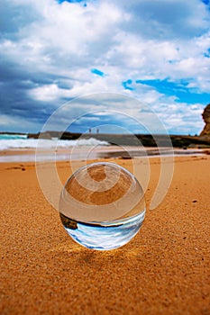 Crystal ball with the upside-down reflection of the sandy beach, the sea and the cloudy sky