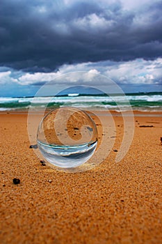 Crystal ball with the upside-down reflection of the sandy beach, the sea and the cloudy sky