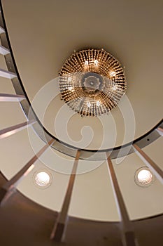 Crystal chandelier on white ceiling with white metal staircase pickets and curving balcony railing photo