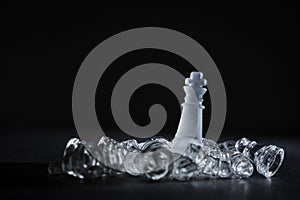 Crystal chess king piece among defeated enemies on a black background with copy space