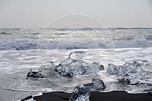 Crystal Clear and Blue Ice Floes on a Black Sand Beach on the Iceland Coast in heavy surf