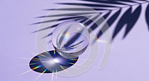 Crystal clear glass sphere on a light lavender background with palm leaf shadow and rainbow light refraction