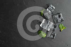 Crystal clear ice cubes with water drops and mint on black table, flat lay. Space for text