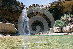 Crystal clear pool of a river with a large waterfall