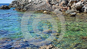 Crystal clear sea water at Limni beach in Corfu, Greece, sea floor with large round stones, and sharp rocks on the shore