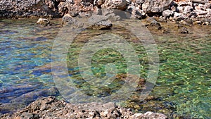 Crystal clear sea water at Limni beach in Corfu, Greece, sea floor with large round stones, and sharp rocks on the shore