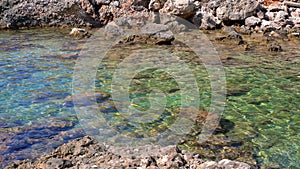 Crystal clear sea water at Limni beach in Corfu, Greece, sea floor with large round stones, and sharp rocks on the shore